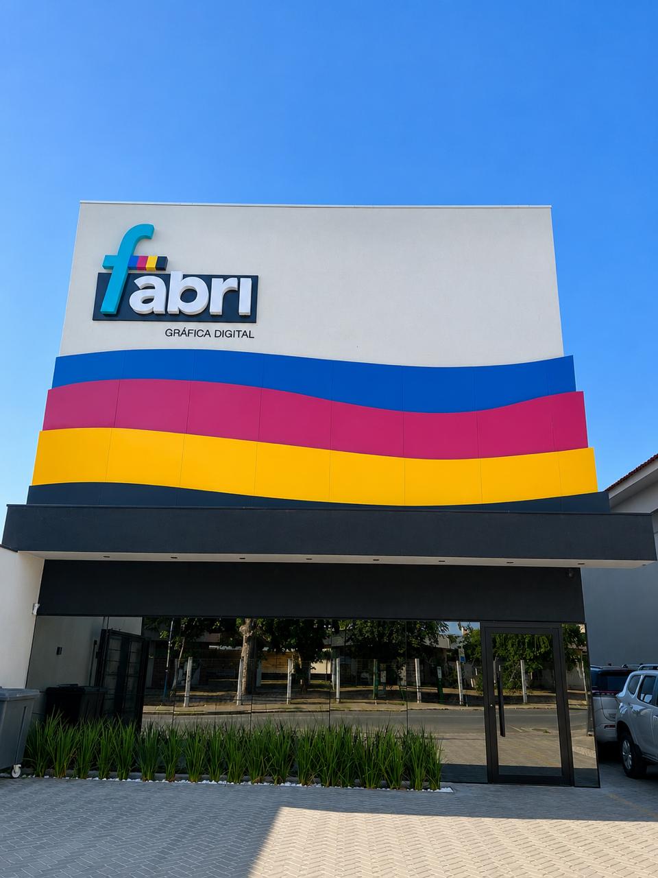 Fachada da Fabri Gráfica Digital em Cuiabá, com faixas nas cores azul, magenta e amarelo